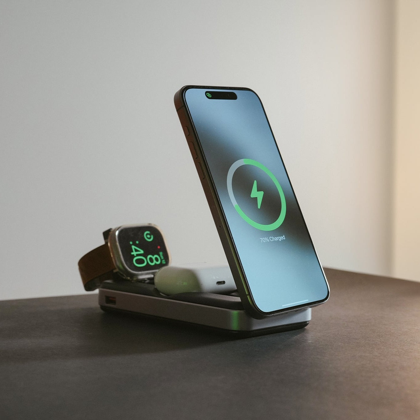 A smartphone and a smartwatch are charging on the Urban PowerBuddy 2.0 5-in-1 Wireless Powerbank, with the phone screen showing 75% charged and the watch displaying 4:40. This ultra-portable charging device keeps your essentials powered up effortlessly.
