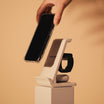 A hand places a smartphone onto the sleek, white Travel S 3 in 1 Wireless Charger - Urban Travel Series stand by Urban, with a black smartwatch positioned in the holder next to it.